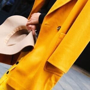 Woman wearing a yellow coat holding a hat